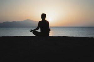 A woman practices meditation with a tranquil ocean sunset backdrop, embodying peace and relaxation.